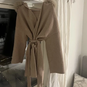 Beige Kappa - Säljer min kappa som är i storlek S. Pälsen är äkta och mjuk. Kappan passar perfekt till nu till våren och går även att ha på hösten/vinter
