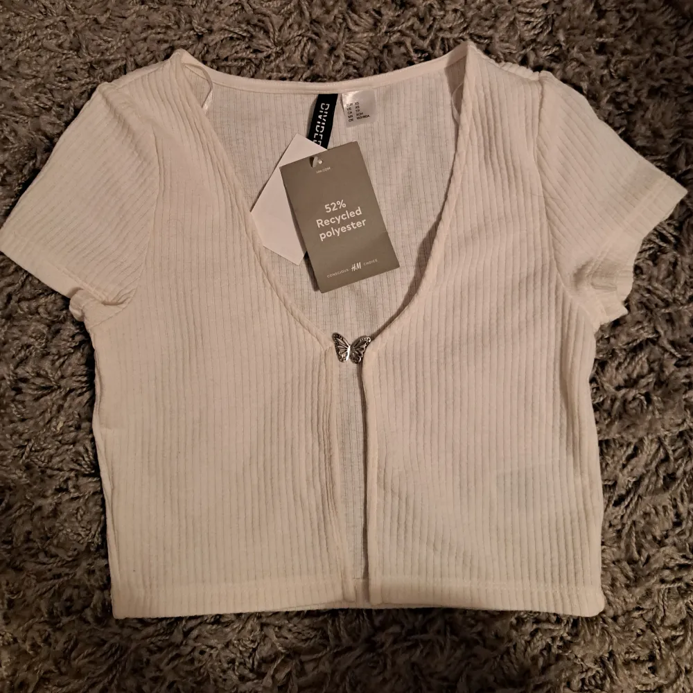 En oavänd t-shirt cardigan som fortfarande har kvar pristaggen. Köptes ifrån H&M men användes aldrig för att jag ångrade mitt köp. Toppen hålls ihop med metall fjärilen och går inte att öppna.  Obs! Köpare står för frakten. T-shirts.