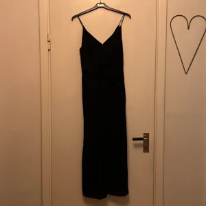 Svartmönstrad festklänning  - Stilig festklänning med liten slits mitt fram. Svart med snyggt möster som ger den en mer exklusiv prägel. 