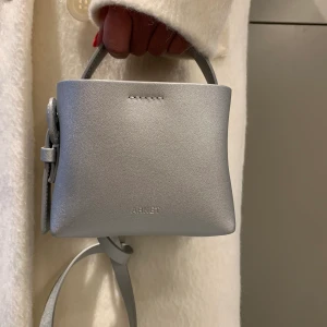 Cool miniväska från Arket - Silverfärgad cool väska från Arket. Knappt använt den så är i nyskick. Köpte för 1200kr, säljer för 600kr!