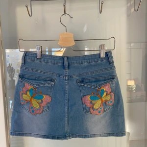 Mini kjol - Mini kjol med fint tryck på bakfickorna, aldrig använd