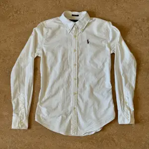 Ralph Lauren slim fit skjorta, använd men i gott skick (vit men inte kritvit längre). Storlek: 0 eller XS, Armhåla till armhåla: 44.5 cm Längd: 64.5 cm Yttre axel till armöppning: 59.5 cm