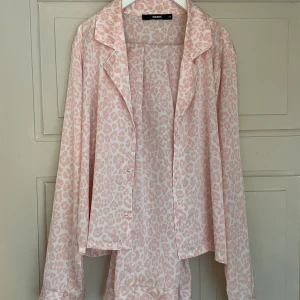 Rosa Pyjamasset - Ett rosa pyjamasset med leopardmönster, skjorta+byxor i skönt silketmaterial. Köpt på BikBok för flera år sen. Säljer då det är en aning för litet och inte kommer till användning. Väldigt bra skick (inga defekter)