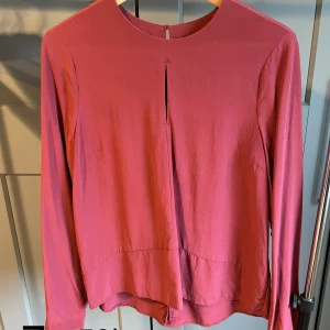 Röd blus  - Röd blus i mycket gott skick. Detaljer med öppna ”sömmar” fram och bak. Knäppa med knapp i bak. 