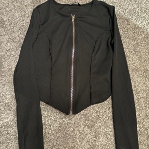 En svart tröja  - Blixtlåset går att dra ner hela vägen. Helt oanvänd.