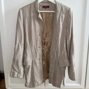 Kavaj/Blazer i en fin beige färg och i linnematerial. Plagget är från märket L.O.G.G och är i storlek 36. 