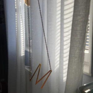 Guldigt halsband (M)  - Säljer det här guldiga halsbandet med ett M på. Väldigt fint nästan aldrig använd. Inga alls defekter men tyvärr så är det inte rostfritt.. 