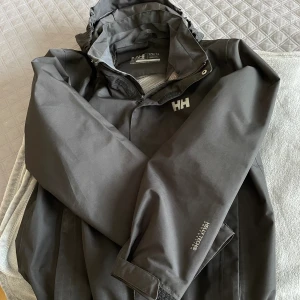 Helly Hansen vindjacka - Säljer denna svarta helly hansen vindjackan som inte säljs längre, köpte den 2019 men har ingen användning då jag har andra jackor. Det står 176 så den är som en lite större S. Finns pyttesmå tecken på slitage. Kan gå ner i pris!