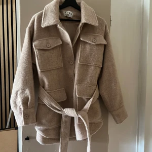  Jacka Oversized - Säljer en jacka från NA-KD, passar på höst och vår. Beige med knappar och bälte i midjan. Jackan är oversize, storlek 36(även oversize om man är storlek 38) Använd 2 gånger förra året. Slutsåld på NA-KD och nypris ligger på 1059kr  