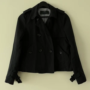 Kort trenchcoat / jacka zara - En kort trenchcoat i mörkblått från zara. Strl xs En knapp saknas på ena sidan, men under kragen så syns inte.