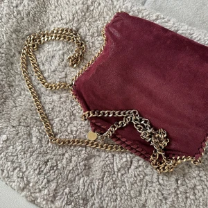 Stella McCartney väska 🍒 - Säljer nu min älskade Stella McChartney väska i modellen mini falabella i en unik vinröd färg med guld detaljer. Äkta med serienummer, däremot slitningar på kedjan samt knappen på insidan av väskan men ingenting som märks!   Skriv för fler frågor!💞