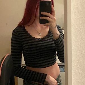 Topp - Långärmad croppad topp som är i randigt mönster med spets runt halsen. Storlek S