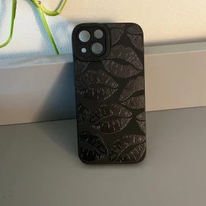 Telefonskal - Ett helt oanvänt telefonskal till iPhone 13 med pussmunnar på i svart. Säljer pga att jag råkat köpa dubbletter. Om du är klantig som mig passar fodralet parfect eftersom det är i ett relativt hårt material! 💗