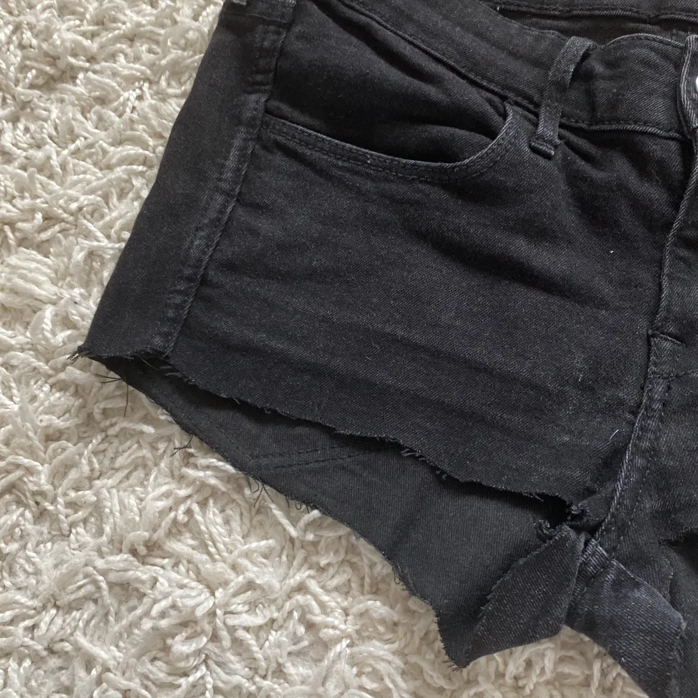 Ett par svarta jeansshorts från H&M med låg midja. Shortsen har en skinny passform och de har en rå kant vid benen och klassiska fyra fickor.. Shorts.