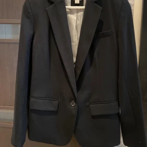 Svart kavaj - En elegant svart kavaj med en enkel knapp framtill och två fickor med lock. Kavajen har en klassisk design med långa ärmar och en Snatched passform.