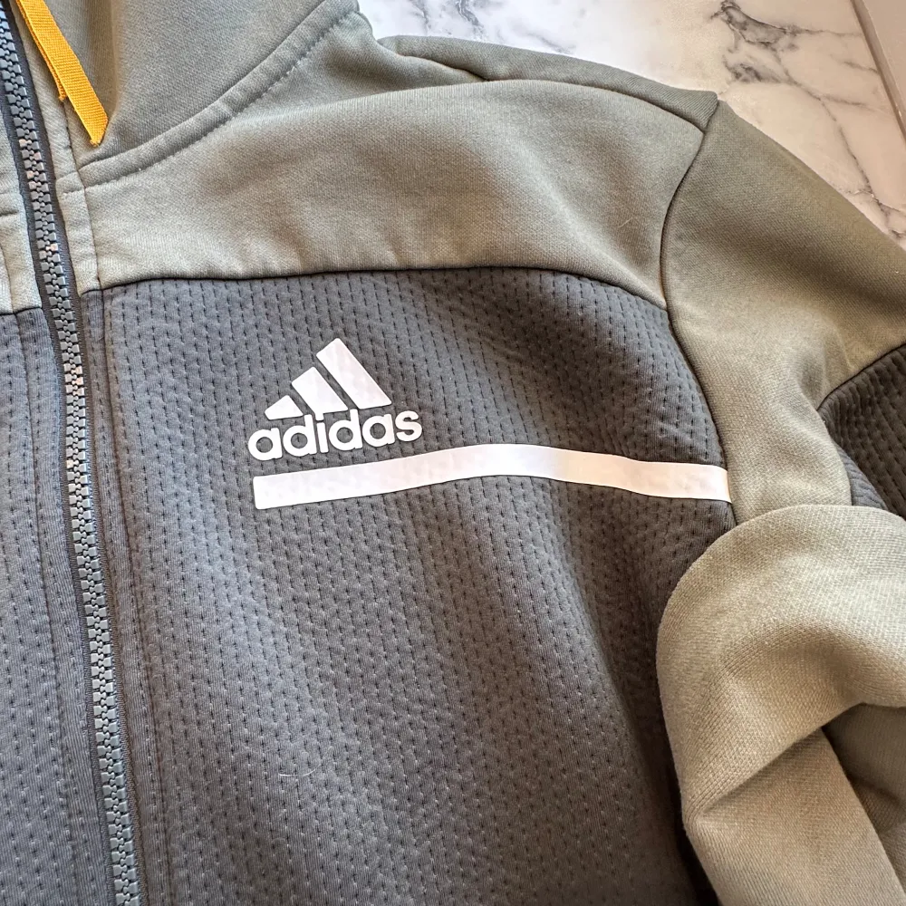 En militärgrön Adidas zip hoodie. Hoodien är luftig och sportig. Kan användas både för träning men även för att använda ute. Den har flera fickor för förvaring av små saker samt en stor luva. Hoodien har endast använts 5-10 gånger och är i gott skick. Hoodies.