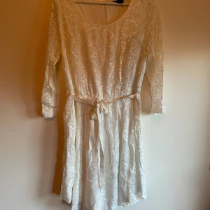 Långärmad spetsklänning - Spetsklänning oanvänd i förpackning. Dragkedja i bak. Genomskinlig spets i ärmarna. 