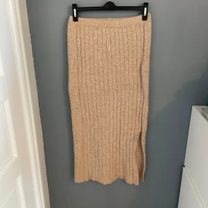 Stickad maxikjol - Beige stickad maxikjol som är ribbad framtill, står ingen strl men skulle säga S/M, resor runt midjan, har en liten slits nertill, går ungefär ner till anklarna men beror på ens längd, aldrig använd🌟🌟