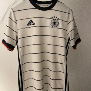 Tyskland fotbollströja EM - En snygg tröja från Tyskland i och med EM 2021.  Tröjan har en liten ”repa” i mitten som syns när man kollar nära men ingenting man annars tänker på, säljs därför till reducerat pris. Köpt på adidas i München Storlek L junior men passar M-S 