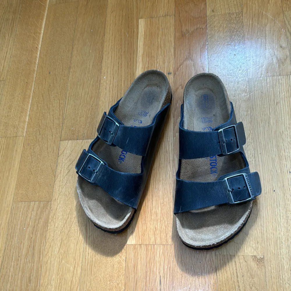 Ett par svarta sandaler från Birkenstock med två justerbara remmar och spännen. Sandalerna har en bekväm fotbädd och en slitstark sula.. Skor.