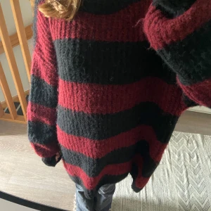 Over sized, långärmad stickad tröja, med röd och svart mönster  - 80 cm längd  60 cm bredd över byst  Lite nopprig  