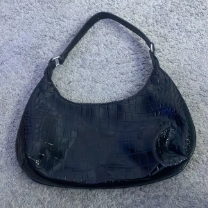 Snygg svart väska 💕 - En snygg handväska i model lite mindre. Crocmönster i svart lack. Perfekt storlek för telefon, solglasögon och andra mindre saker man vill få med sig! Använd 1 gång ( nyskick ). 