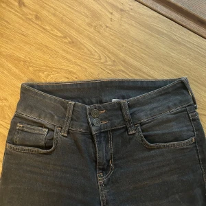 Lågmidjade jeans - Lågmidjade jeans i storlek 36. Högtid detalj vid gylfen och fickorna. Brun/grå i färgen. Bootcut i passform. Innebenslängd:78 cm