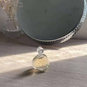 Parfym i rund flaska - En elegant parfym i en rund, genomskinlig flaska med en klar vätska. Flaskan har en dekorativ, rund kork. Toppnoterna inkluderar päron, rosa peppar, svarta vinbär och bergamott. Mellannoterna består av gardenia och egyptisk jasmin. Basnoterna är amber, mysk och patchouli.