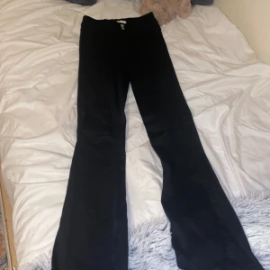 Svarta Jeans - Svarta byxor med  utsvängd och bootcut-stil. Byxorna har en dragkedja och knappar framtill.