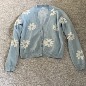 Blå cardigan - Blå cardigan med vita blommor. Otroligt mjuk och skön. Är i storlek 170 men den passar som en S. Aldrig använd och finns inga defekter.