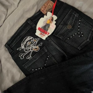 Lågmidjade svarta jeans med broderad design - Svarta oanvända jeans med en broderad döskalle på bakfickan. Fickorna är dekorerade med nitar. Rak modell, storlek S, lågmidjade. Jag är 167, har dock ingen rättvis bild då de är försmå. Midjemått 80cm Innerbenslängd 82cm  