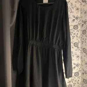 Svart långärmad klänning - Säljer en elegant svart klänning med långa ärmar. Klänningen har en enkel och stilren design med en markerad midja som ger en fin passform. Perfekt för både vardag och festliga tillfällen. Passar bra till höst och vinter.