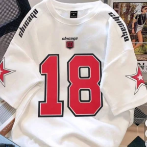 Vit t-shirt med tryck från Chicago - Säljer en vit t-shirt med tryck från Chicago. Den har stora röda siffror '18' på framsidan och svarta textdetaljer på axlarna. På ärmarna finns röda stjärnor med vita konturer. Perfekt för en sportig look eller casual vardagsstil. T-shirten är i nyskick och gjord av bomull.