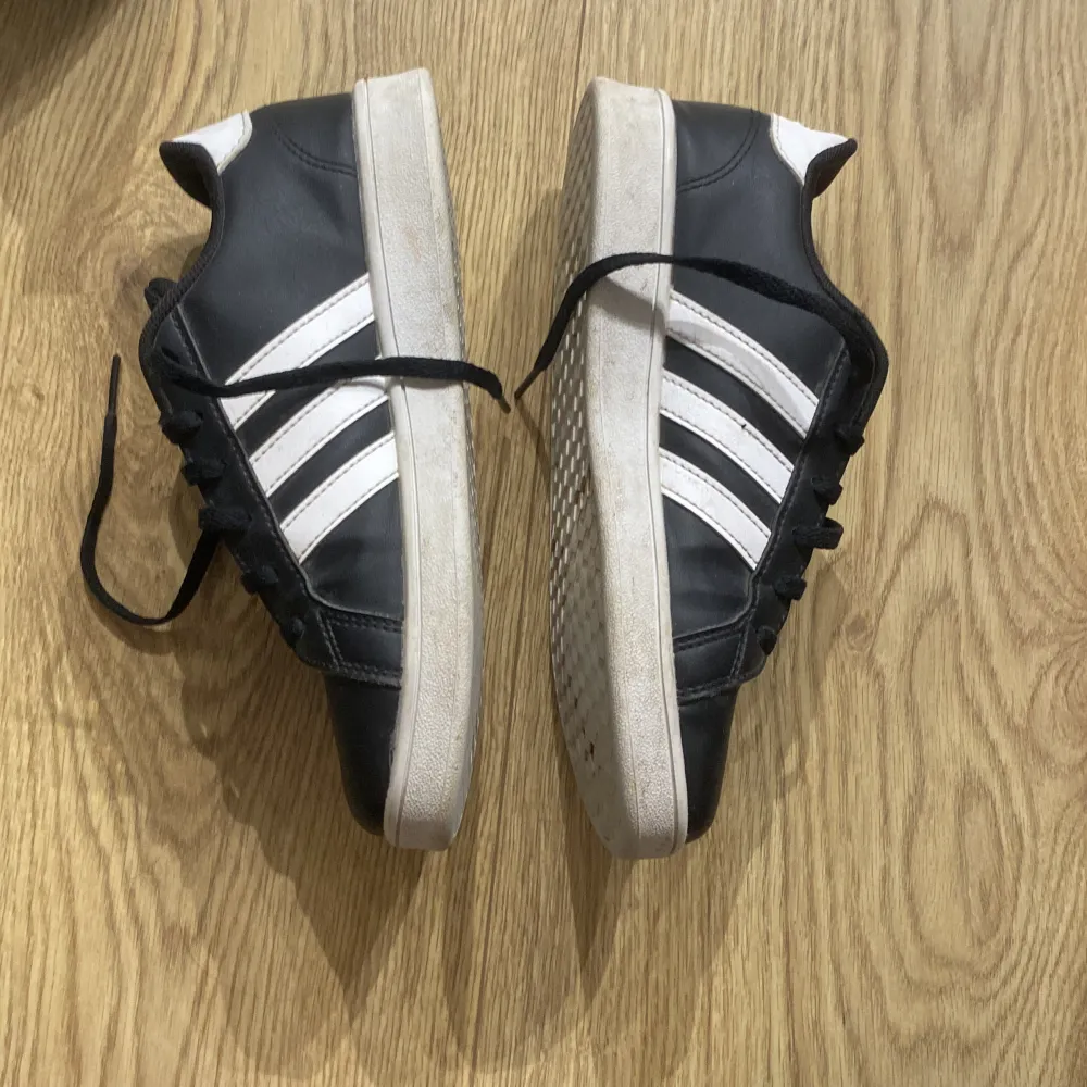 Säljer ett par svarta Adidas sneakers med de klassiska vita ränderna på sidorna. Skorna har snörning och en vit sula som är lite smutsig men annars i bra skick. Perfekta för vardagsbruk och passar till det mesta i garderoben.pris kan som vanligt diskuteras💗. Skor.