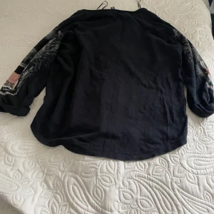 Svart tröja med pantermotiv på ärmarna - Säljer en cool svart tröja med ett häftigt pantermotiv på ärmarna. Tröjan är långärmad och perfekt för höst och vinter. Den är i bra skick och passar perfekt för en avslappnad stil. Perfekt för dig som vill ha något unikt i garderoben! Har fått den av min kusin så den är lite använda sen innan men jag har aldrig använt den🥰