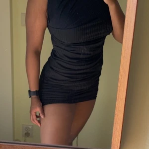 Svart klänning  - Baksidan: 90cm lång  Framsida: 106cm lång  Använd 1 gång  Svart klänning med en figursydd passform. Klänningen har en hög hals och är utan ärmar. Egentligen lång klänning men jag är så kort så jag har dragit upp den lite  Storlek 40/M