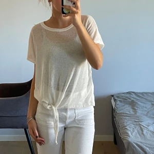 Stickad t-shirt - Stickad vit t-shirt som man kan knyta där nere. Bra skick. Skulle säga att den passar s-m beroende på hur man önskar passformen. 