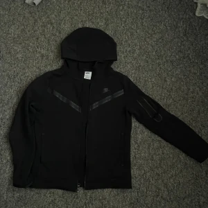 Svart jacka från Nike - En svart Nike tech fleece med huva och dragkedja. Blivit för liten därför behöver den en ny ägare(sms vid intresse av köp😊