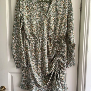 Blommig klänning från Rut&Circle - En vacker blommig klänning från Rut&Circle i storlek S. Klänningen har långa ärmar och en omlott-design med rynkade detaljer på sidan. Den har en v-ringad hals och är perfekt för vår- och sommarsäsongen.