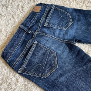 Vintage American Eagle jeans - Lågmidjad och slim bootcut modell med assnygga paljettdetaljer där bak. 😍 Perfekt skick, förutom att de är uppsydda vilket inte syns. 🫶🏻 Mått på bilder, men kan fixa fler i DMs. Jag är 167. ❤️ Håll koll på min profil, har flera snygga jeans uppe! 🥰