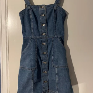 Jeansklänning  - Söt jeansklänning, ej använd ofta. Justerbara axelband, knapparna går att knäpp upp. Mjuk och skön för att vara jeans 