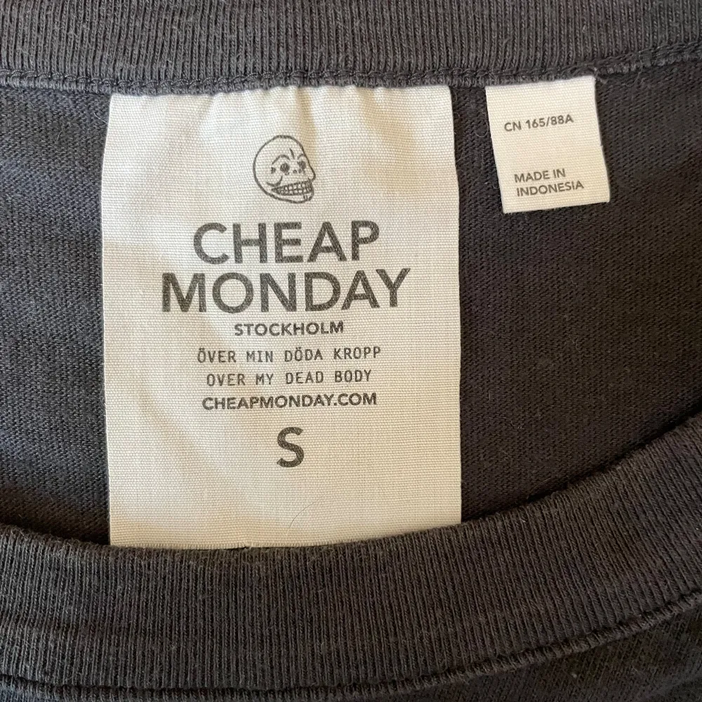 Svart klänning med tryck på baksidan av märket Cheap Monday. Rund halsringning och korta ärmar med axelvaddar (går att ta ur).. Klänningar.