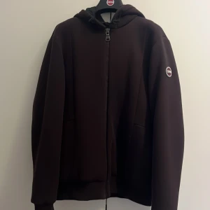 Mörkbrun jacka från Colmar - En mörkbrun jacka från Colmar med dragkedja och huva. Jackan har en enkel design med Colmar-logotypen på vänster ärm.