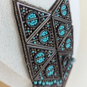 Halsband med turkosa pärlor och fransar - Ett vackert halsband med en triangulär hängsmycke dekorerat med turkosa pärlor och metalliska detaljer. Halsbandet har en kedja och fransar som hänger ned från smycket, vilket ger det en bohemisk känsla.
