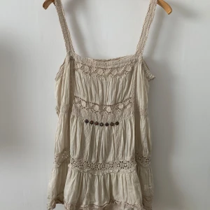 Odd Molly beige topp, stl S/M - En söt och romantisk topp med spetsdetaljer och knappar. Toppen har en lös passform och är perfekt för varma sommardagar.    Skick: Ok, Den har en liten skada på  spetsen vid ena axeln, går nog att laga, se bild  Stl: S/M Längd: 59cm 