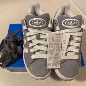 Nya gråa Adidas Campus 00s -storlek 38 - Adidas Originals Campus 00 s j 38. Grå (Grey Three) Ingår både vita och gråa skosnören.Nya och oanvända. Ligger kvar i kartong. Köpta i svensk webbutik och kommer inte från någon massimport utomlands. Därmed 100% äkta. Sista paret!