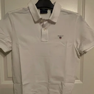 Piké-tröja Gant - Vit piké-tröja från Gant med ett märke på vänster bröst samt två knappar upptill. Fint skick.