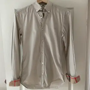 En väldigt fin skjorta från burberry,den är i biege färg och är nästan helt ny använd 4-5 gånger. Nypris 5600kr mitt pris 899.