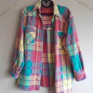 Regnbågsfärgad flanelkskjorta - Fantastisk skjorta I blandade färger, med silverknappar & dekorativa sömmar. Köpt på en vintagemässa i Berlin. Använd enstaka gånger. Ej storleksmärkt, jag uppskattat den till M/L.  Katt finns i hemmet. Önskar du fler bilder? Skriv till mig! 🌼