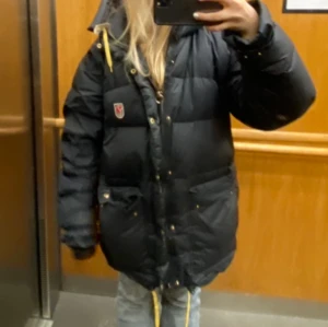 Svart fjällräven jacka  - Säljer denna jättefina fjällräven jacka! Den är svart och är i storlek L tror jag. Den är i helt okej skick, det finns ett hål i armen och några av de gula banden har åkt av men annars är den annars jättefin !! 